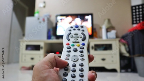 man holding remote control of a television. man watching television. selective focus at the middle button of television remote. blurred background