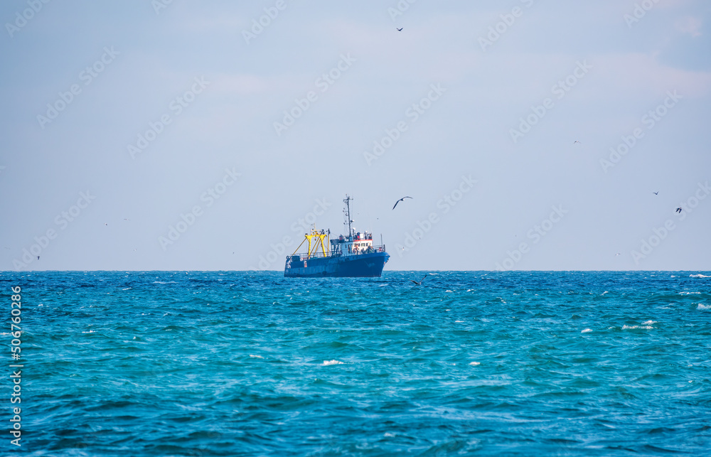 Fishing boat in blue sea and clear sky with birds flying overhead.