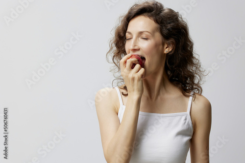 Enjoyed cheerful lovely curly beautiful woman in basic white t-shirt enjoy fresh apple fruit posing isolated on over white background. Natural Eco-friendly products concept. Copy space