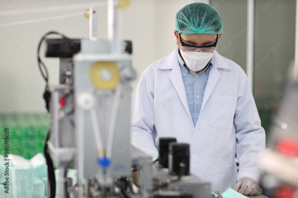 Worker in personal protective equipment or PPE inspecting quality of mask and medical face mask production line in factory, manufacturing industry and factory concept. Worker in personal protective equipment or PPE inspecting quality of mask and medical face mask production line in factory, manufacturing industry and factory concept.