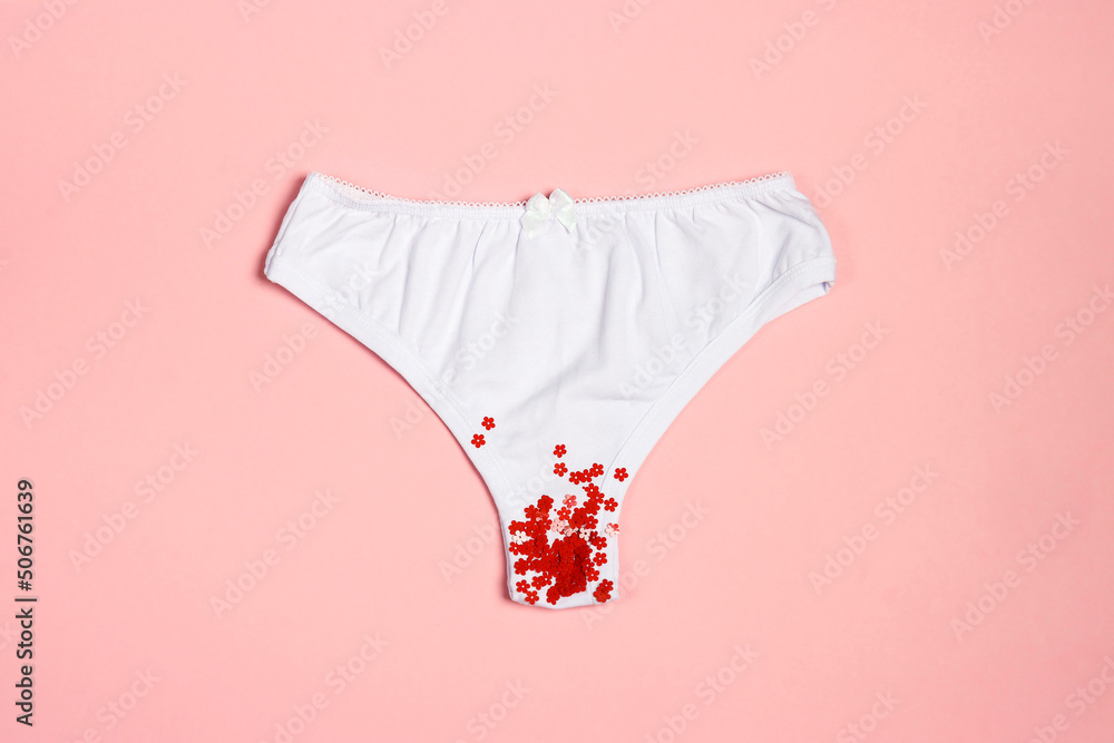 White women's panties with red flower sequins on a pastel pink background. - obrazy, fototapety, plakaty 