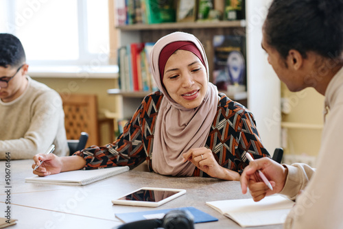 Obraz na plátně Muslim woman wearing hijab sitting at table in library taking look into notebook