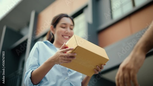 Close up parcel in hand of blue uniform delivery man to customer front of the house with good service from shopping online. Courier man delivering a cardboard box postal package to destination. photo