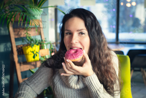 Portrait of an attractive woman in a cafe with a doughnut. Winter  warm clothes  coffee and sweets. Front view.