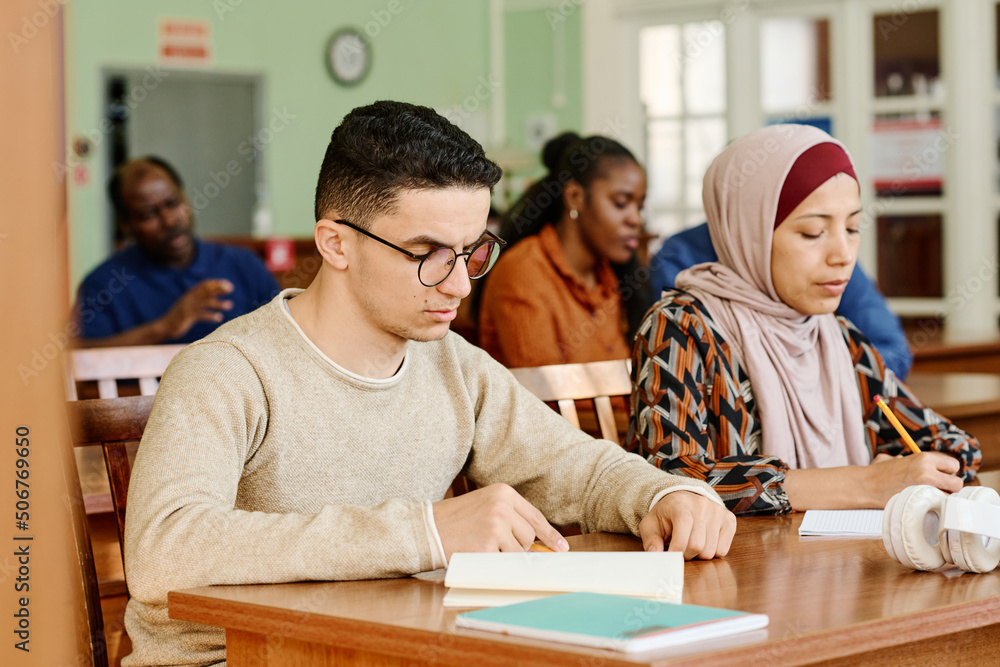 Group of immigrant students in international class sitting at desk reading and making notes during lesson Group of immigrant students in international class sitting at desk reading and making notes during lesson