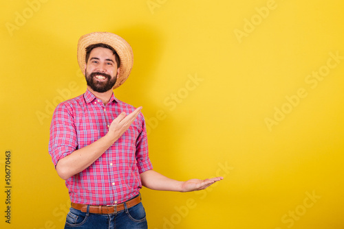 Bearded man wearing typical clothes for party Junina. presenting with hands. negative advertising space and text. For the Arraia Party photo