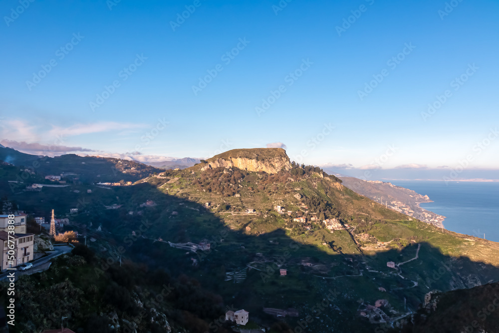 Panoramic view on Monte Ziretto and the coastline seen from Taormina, Sicily, Italy, Europe, EU. Sunset time at the Ionian Mediterranean sea. Hill landscape along the small coastal villages, towns