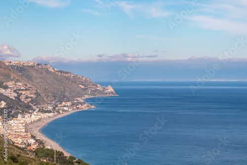 Panoramic view on the coastline seen from Taormina, island Sicily, Italy, Europe, EU. Sunny vacation day at the Ionian Mediterranean sea. Hill landscape along the small coastal villages, towns