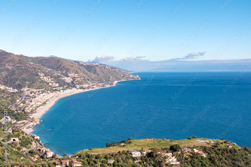 Panoramic view on the coastline seen from Taormina, island Sicily, Italy, Europe, EU. Sunny vacation day at the Ionian Mediterranean sea. Hill landscape along the small coastal villages, towns