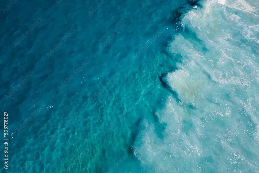 Top view of blue transparent water in ocean and foam by waves, aerial drone view