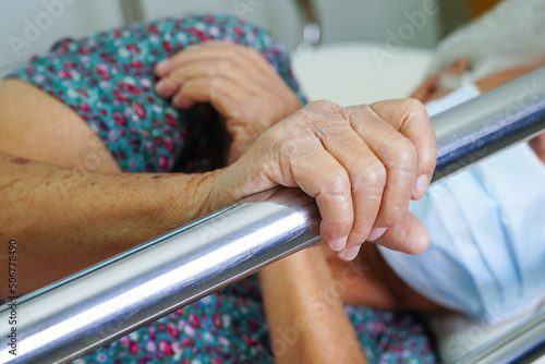 Asian elder senior woman patient holding bed rail while lie down with hope waiting her family in hospital.