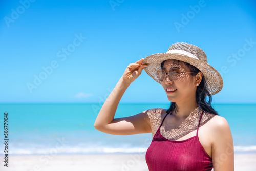 Young women in bikini and straw hat stand on tropical beach enjoying looking view of beach ocean on hot summer day. Blue sea in background. Khao Lak, Phang Nga, Thailand. Summer vacation concept © TripleP Studio