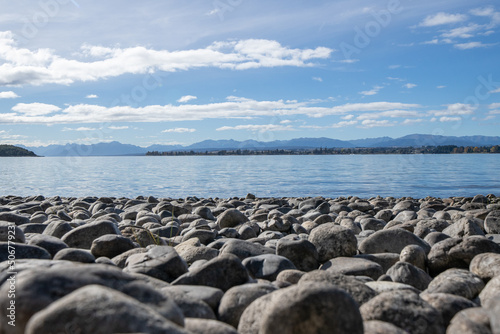 Rocky foreshore of Lake Te Anau with view to other side and few clouds in sky.