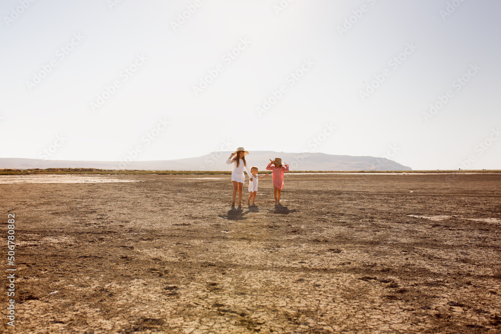 three children hold hands and run together deserted beach, dried-up mud lake. Summer children's recreation in nature. Children in tunic dresses from the sun, three children hold hands and run together deserted beach, dried-up mud lake. Summer children's recreation in nature. Children in tunic dresses from the sun,