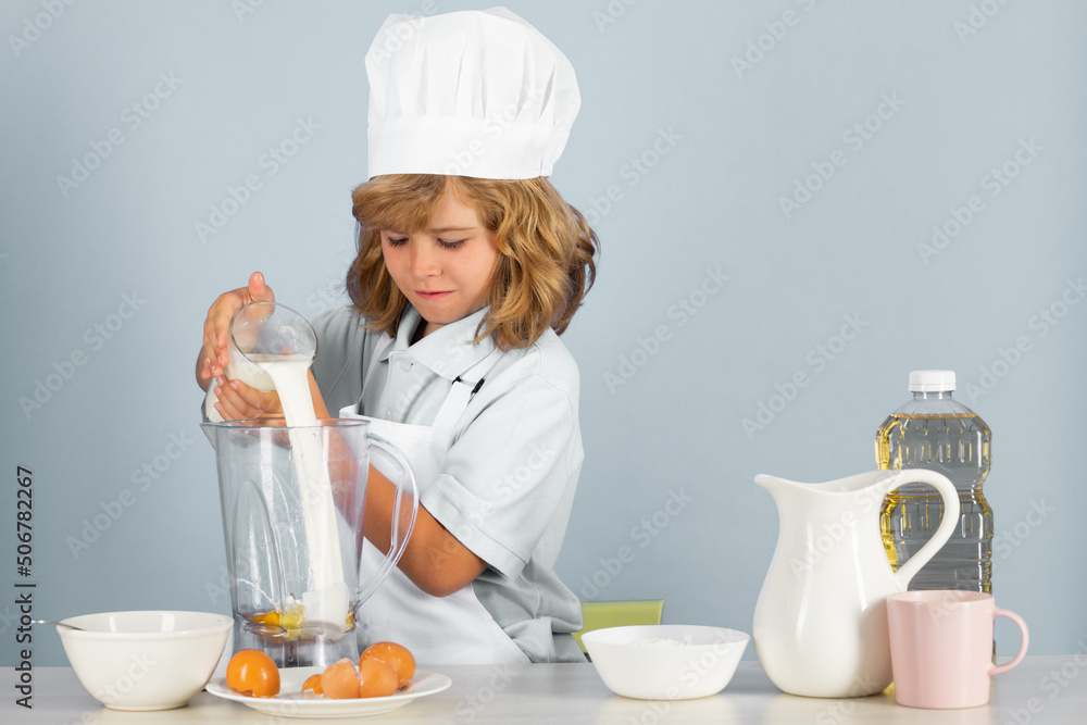 Portrait of a 7, 8 years old child in cook cap and apron making fruit salad and cooking food in kitchen. Cute little blonde happy smiling chef. Portrait of a 7, 8 years old child in cook cap and apron making fruit salad and cooking food in kitchen. Cute little blonde happy smiling chef.