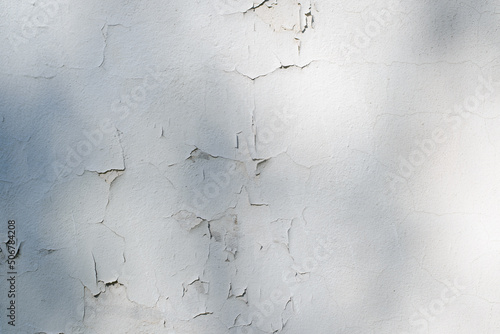 White cracked paint on concrete wall with shadows, outdoors. Texture empty background