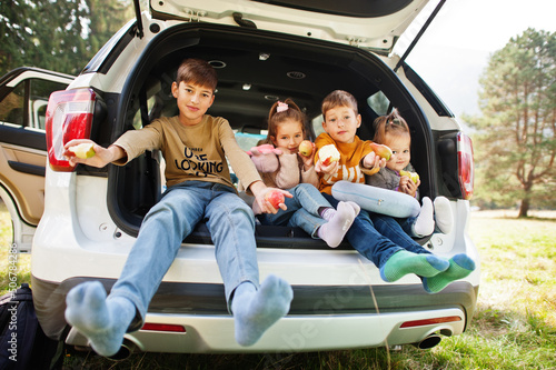 Family of four kids eat apples at vehicle interior. Children sitting in trunk. Traveling by car in the mountains, atmosphere concept. © AS Photo Family