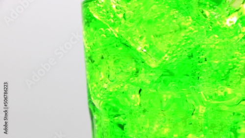 Green sparkling water with Ice in glass. Rotate glass of Green sparkling water drink over white background.