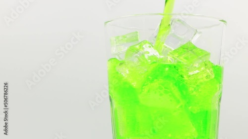 Pouring Green sparkling water with ice cubes close-up. Green sparkling water with Ice in glass. Rotate glass of Green sparkling water drink over white background.