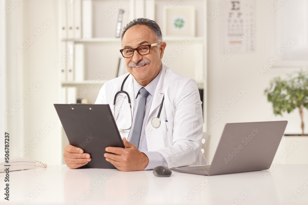 Mature doctor sitting in an office in front of a laptop computer Mature doctor sitting in an office in front of a laptop computer