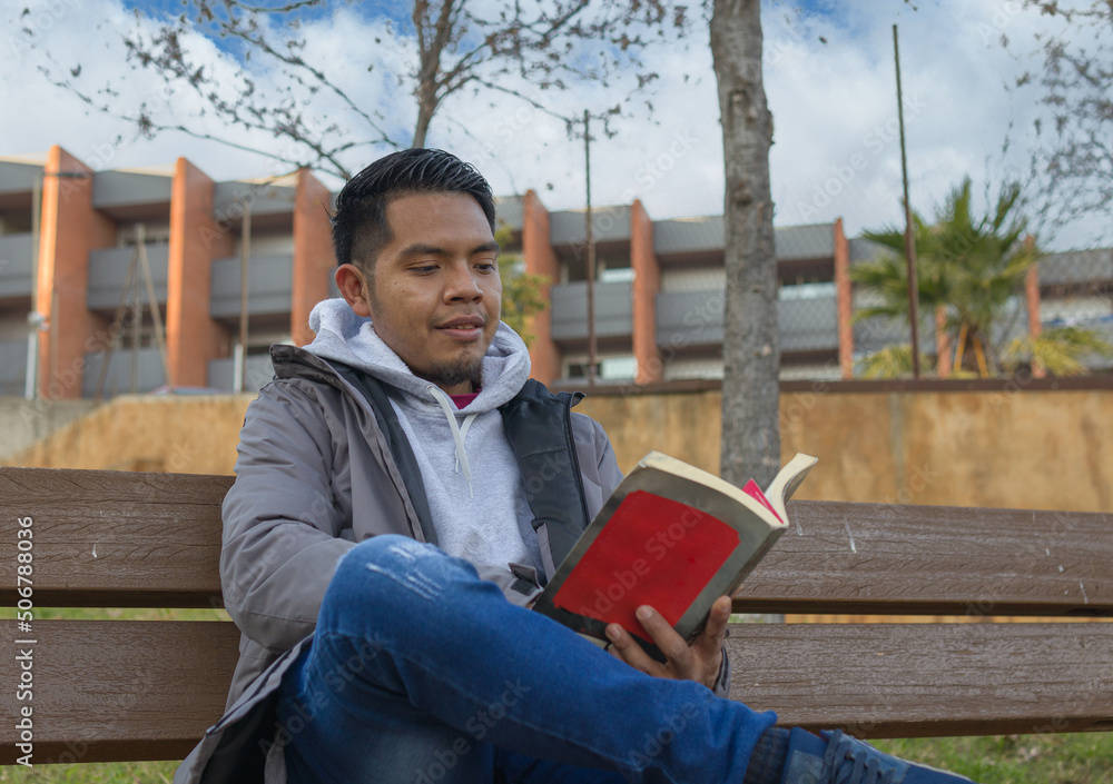 close up shot of a hispanic young man reading a book sitting on a park bench close up shot of a hispanic young man reading a book sitting on a park bench