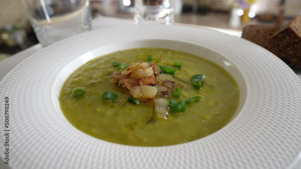Green pea cream soup in white plate with spices on the table, rotate, close up. Healthy food, delicious dried green pea soup Green pea cream soup in white plate with spices on the table, rotate, close up. Healthy food, delicious dried green pea soup