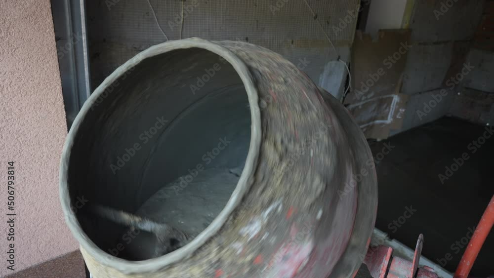 Worker pours rubble and sand into a old dirty concrete mixer at a construction site with a shovel, close up. Building site. Concrete mixer spinning on a construction site Worker pours rubble and sand into a old dirty concrete mixer at a construction site with a shovel, close up. Building site. Concrete mixer spinning on a construction site