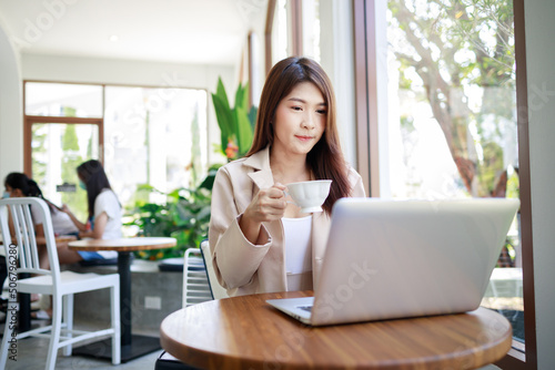 Smart Asian businesswoman drinking coffee and working by computer laptop in the coffee shop