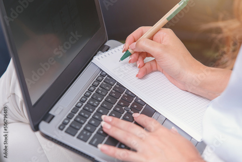 woman working on a laptop in the office writes something in a notebook