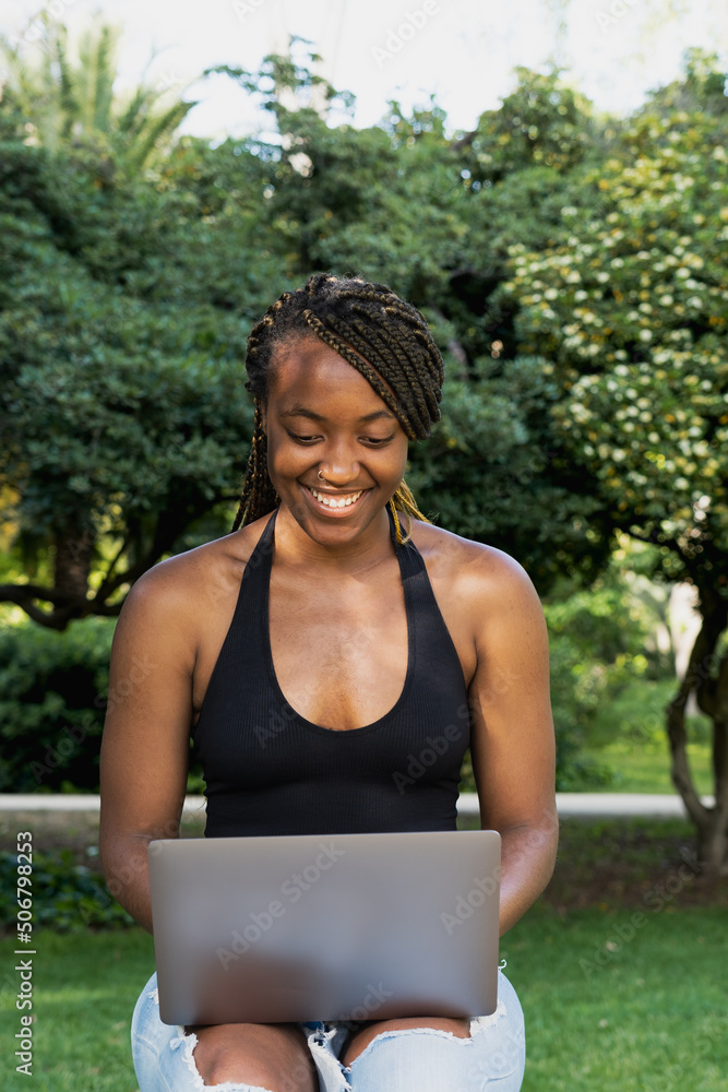 Young African American woman sitting on a bench, using a laptop computer. Young African American woman sitting on a bench, using a laptop computer.