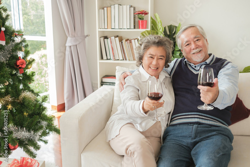 Couple of love elderly asian senior man woman happy with smile and holding glass of wine, hugging together in living room that decorated for Christmas festival holiday concept