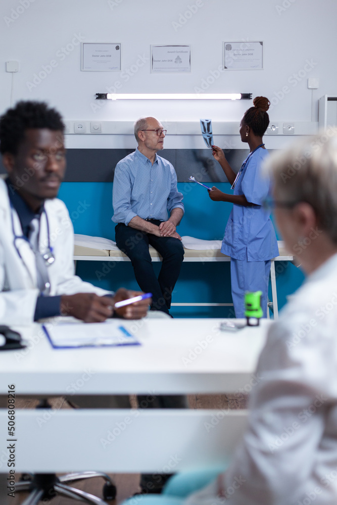 Healthcare facility nurse examining x-ray scan image of elderly patient with acute leg pain. Retired man listening to nurse talking about consultation appointment and treatment schedule Healthcare facility nurse examining x-ray scan image of elderly patient with acute leg pain. Retired man listening to nurse talking about consultation appointment and treatment schedule