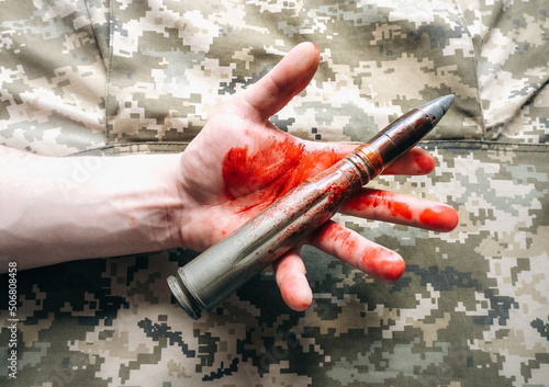 Shell missiles with blood in mans hand on khaki jacket background. No war, army concept.