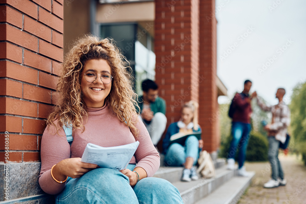 Happy female student learns while relaxing on steps at campus and looking at camera. Happy female student learns while relaxing on steps at campus and looking at camera.