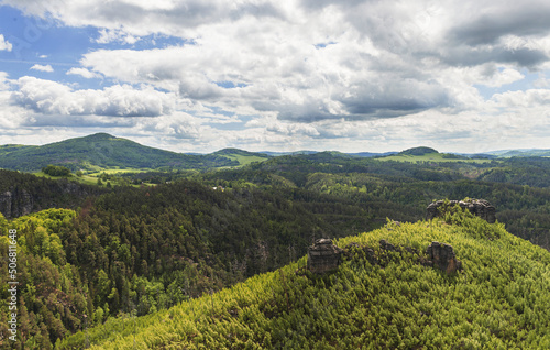 Beautiful view of the landscape of Bohemian Switzerland. The photo shows rocks between trees and clouds in an otherwise blue sky. The photo is taken from the top of Maria Rock. © Photoisfundude