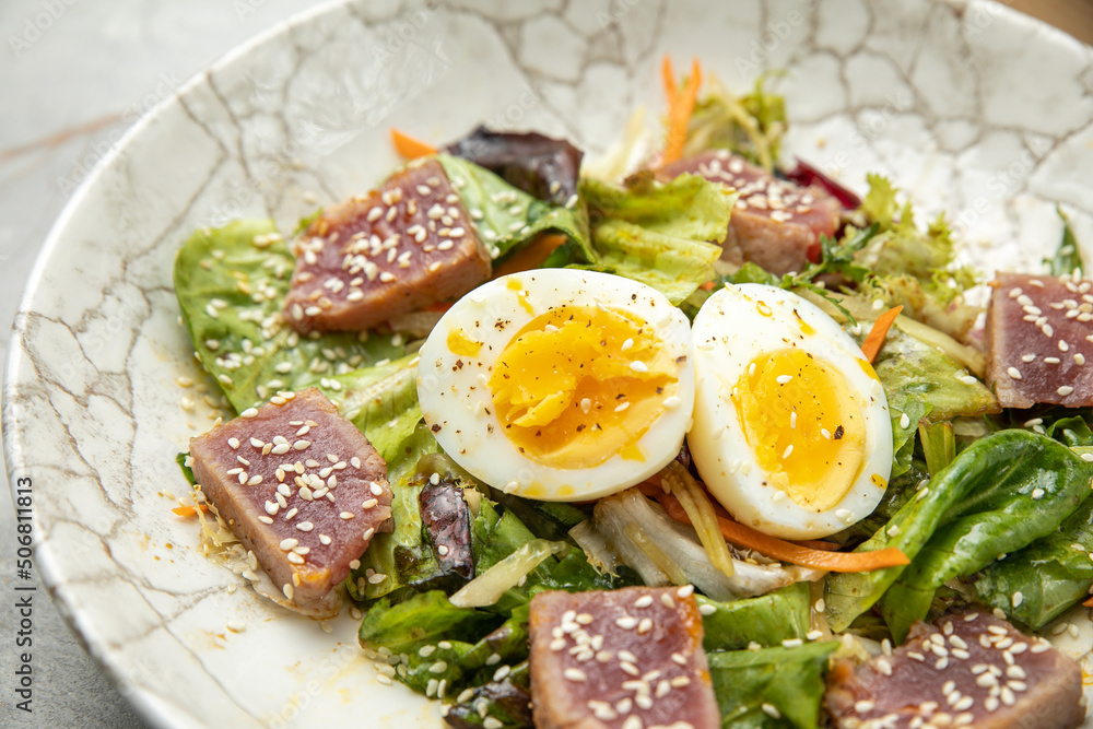 salad with tuna, lettuce, herbs, egg, on a gray table
