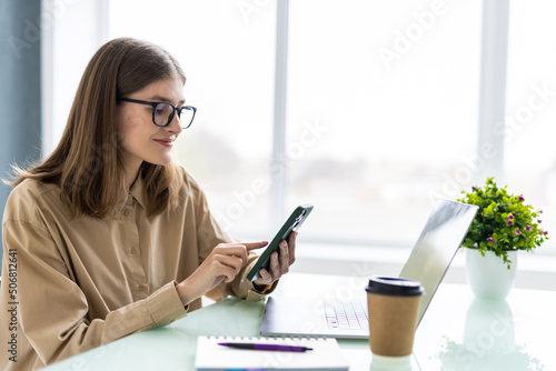 Photos Young woman working from home using phone and computer, woman's hands using smar