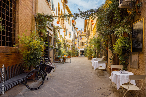 Fototapeta Naklejka Na Ścianę i Meble -  Beautifully landscaped narrow street with restaurant tables in the old town of Grosseto, in Maremma region of Italy. Cozy city view of the old Italian town