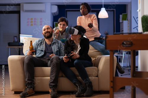 Multiethnic group of people having fun with video games on console and virtual reality glasses. Coworkers meeting at office party celebration with beer drinks after work hours.