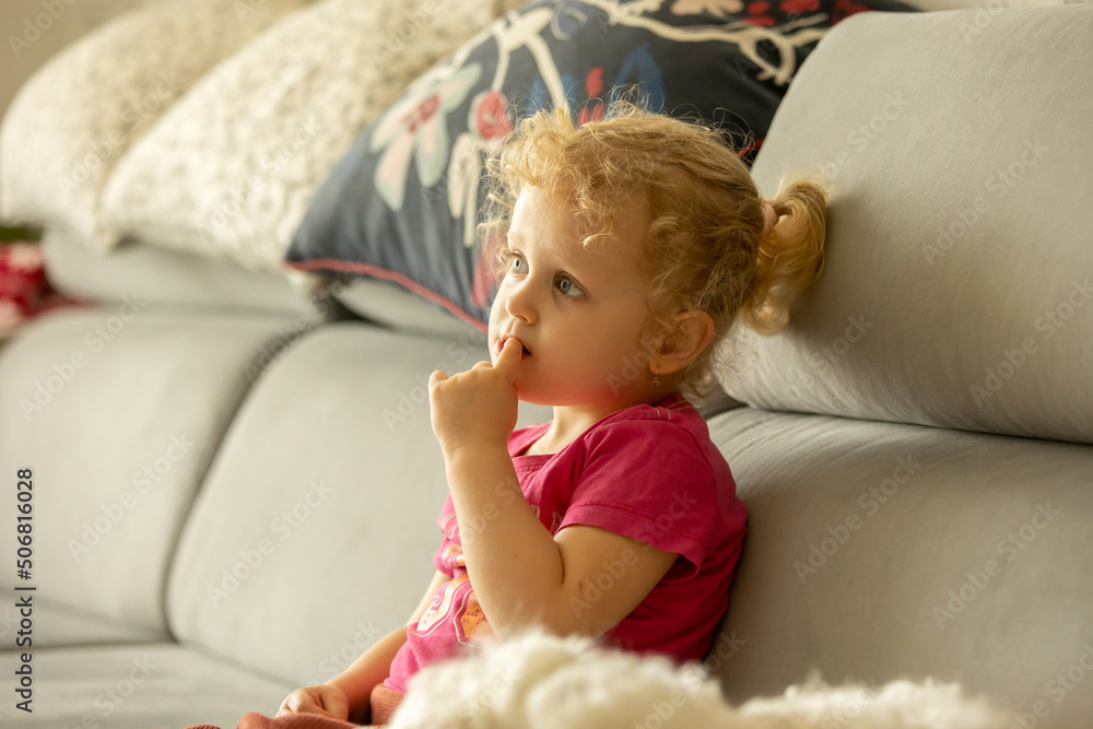 Fototapeta premium Cute little blond toddler girl, sitting in front of the TV with popcorn, watching movie with her pet dog