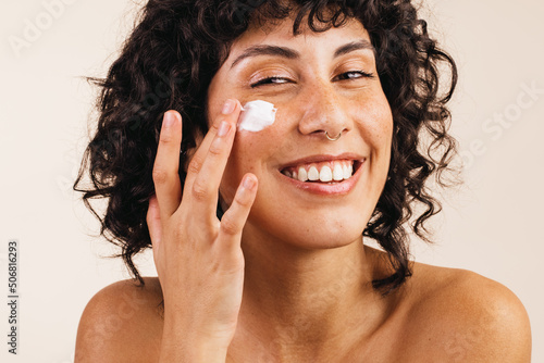 Photos Attractive young woman applying moisturizing cream on her face