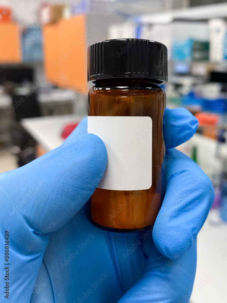 A researcher holding an amber glass vial with white powder inside