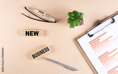 NEW BUSINESS text on wooden block with chart and glasses, business concept