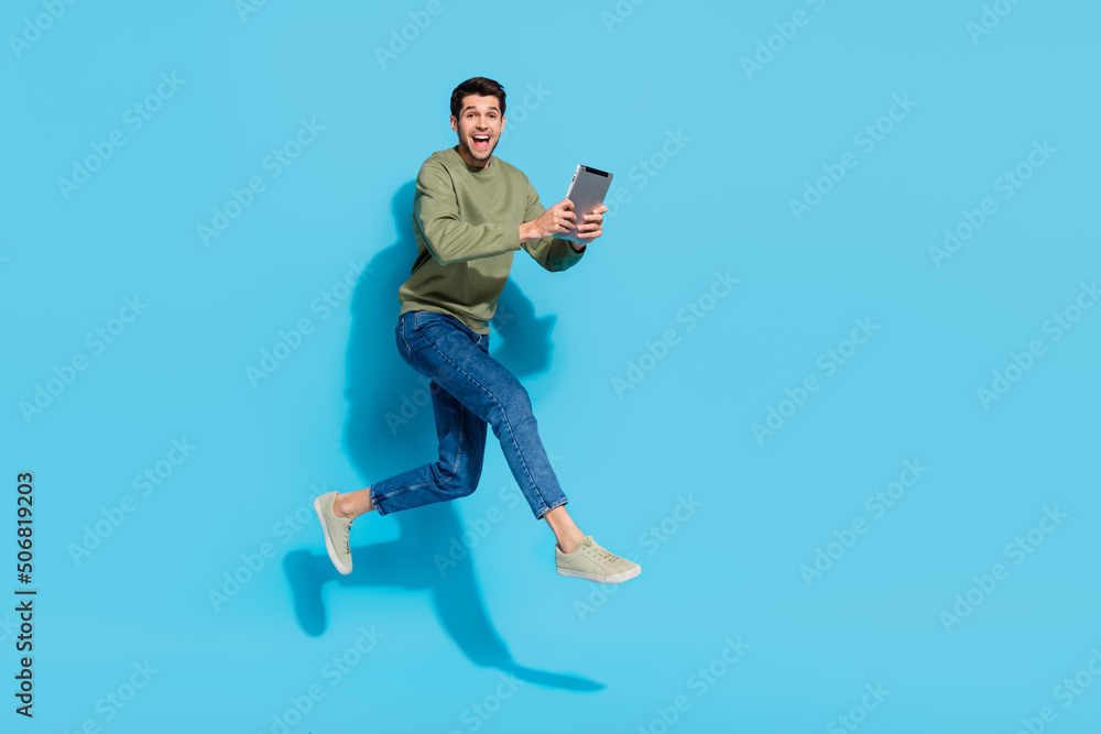 Obraz premium Full size photo of cheerful person jump hold tablet run rush fast isolate don blue color background