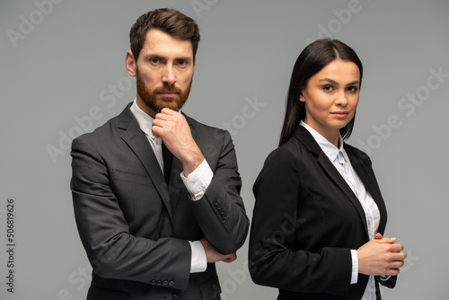 Concept of partnership in business. Young man and woman standing near each other against grey background. Stock photo
