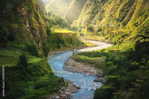 Colorful landscape with high Himalayan mountains, beautiful curving river, green forest, grass, yellow sunlight at sunrise in summer. Mountain canyon in Nepal in spring. Travel in Himalayas. Nature