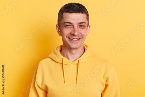 Horizontal shot of delighted man wearing casual style hoodie posing isolated over yellow background, standing with happy facial expression, being in good mood.