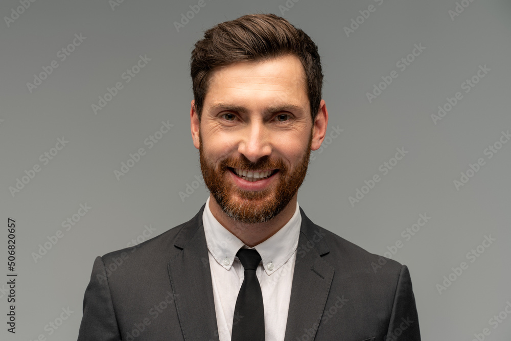 Isolated shot of young handsome male with beard and trendy hairdo, wearing formal clothes posing with toothy smile in studio against grey background Isolated shot of young handsome male with beard and trendy hairdo, wearing formal clothes posing with toothy smile in studio against grey background
