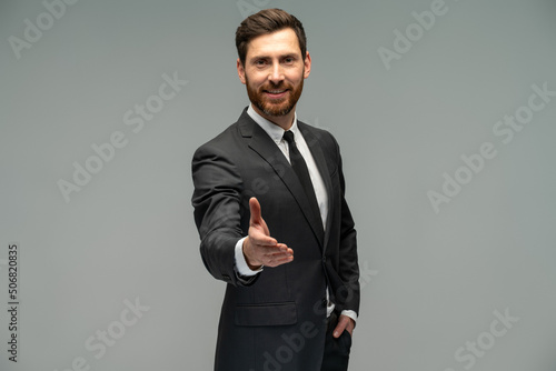 Male businessman in a suit stretching hand and shows a palm up gesture on a grey background. Concept of request, handshake