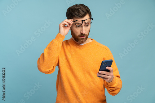 Mobile connection. Portrait of shocked astonished man reading post on social network using cell phone, chatting looking surprised. Indoor studio shot isolated on blue background